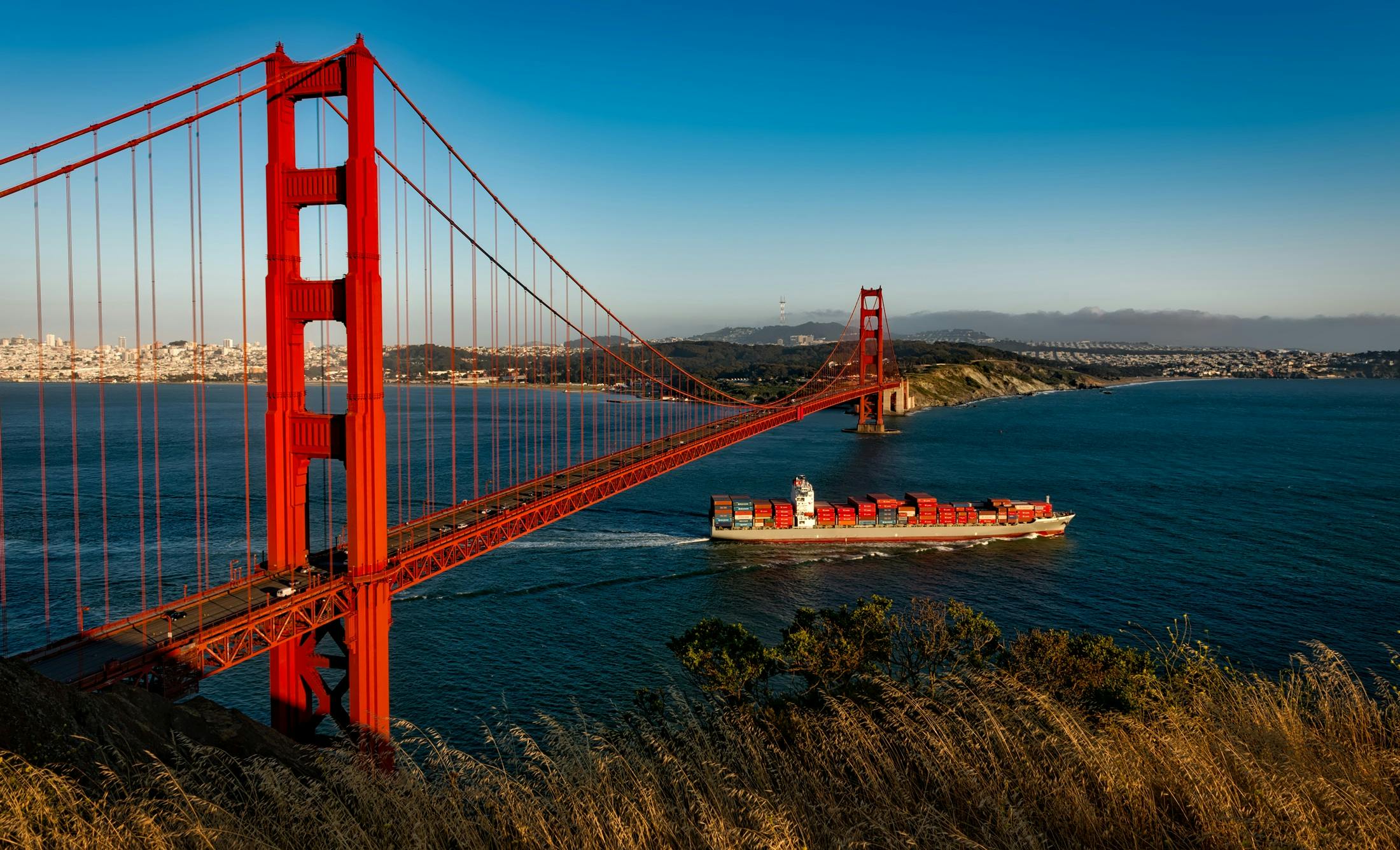 Cargo ship crossing under the golden gate bridge representing trade and tourism